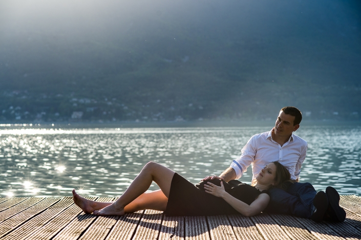 Couple de futurs parents sur un ponton au lac du Bourget, la future maman allongée, la tête sur les cuisses du future papa